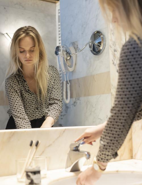Junge Frau im Badezimmer aus Marmor, spiegelt sich im großen Badspiegel beim Händewaschen