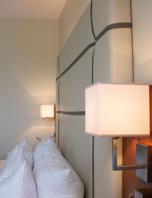 gemütliches Bett im Doppelzimmer mit cremefarbenem Bettkopfteil sowie Leselampen und Lampenschirmen